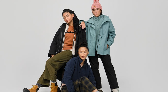Image of three young women in full Timberland outfits in shades of blue, navy, orange, green and black.