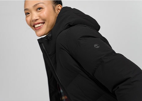 Image of a smiling young woman in a black Timberland puffer coat.