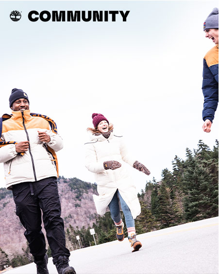 Image of three young people in Timberland puffy coats and hats walking down a snowy street with evergreen trees and mountains in the background. 