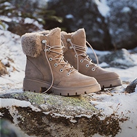 A pair of light brown Timberland Boots sitting alone in the wilderness on a small rock, still looking rugged yet very fashionable.