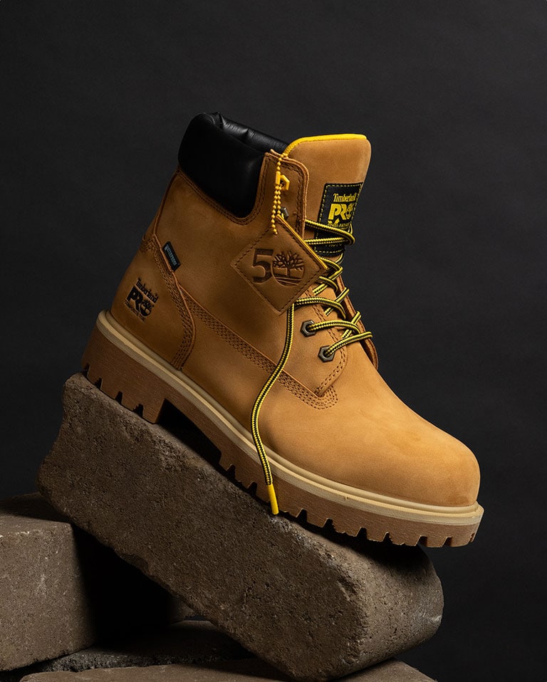 Images cycle through different Timberland PRO work boots, propped on a stand with black background. Each workboot is untied - one is completely wheat colored, one is wheat with large white outsoles and one is black. These boots honor the 50th anniversary of Timberland.