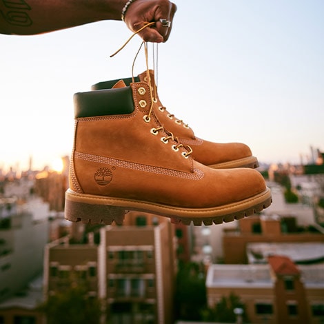 Man holding Timberland Boots with city in background.