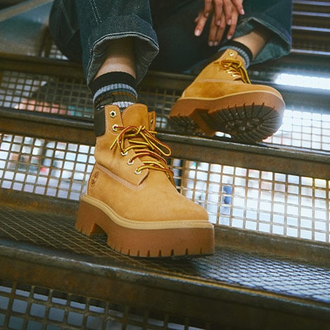 Woman wearing Timberland boots and jeans while sitting staircase.