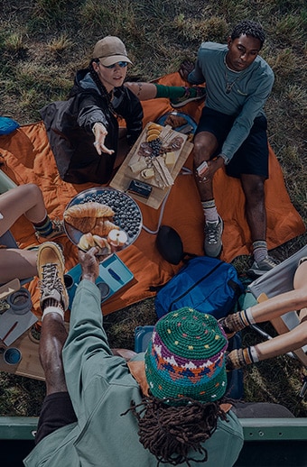 Friends sitting around a blanket, camping and sharing a charcuterie. 