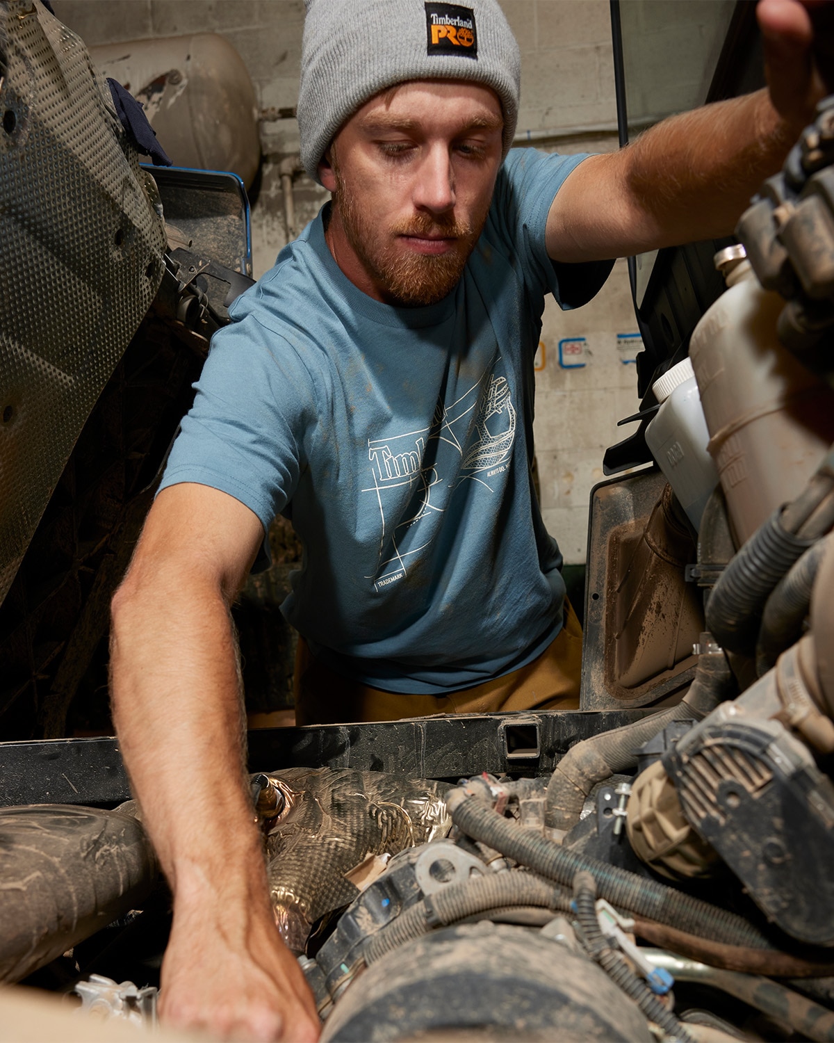 image of a man wearing a gray beanie and a blue t-shirt working on a car