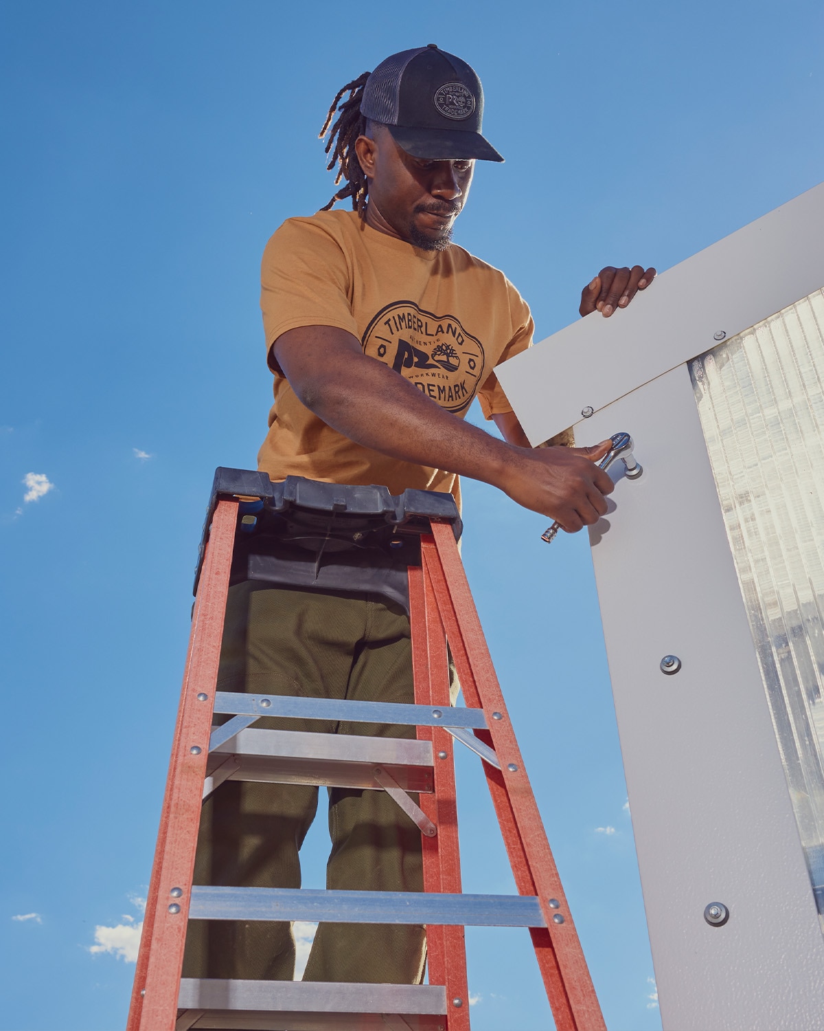 image of man wearing a yellow shirt and a cap standing on a ladder doing work