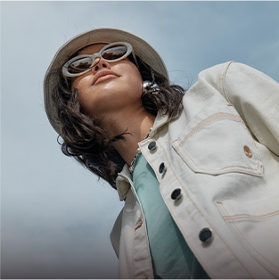 woman wearing a white denim jacket, bucket hat, and white sunglasses