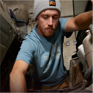 image of man wearing a light blue Timberland shirt and Timberland PRO beanie working on a car