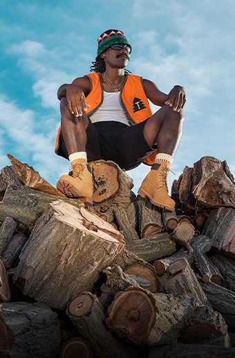 Man sitting on a pile of logs wearing Timberland Yellow Boots.